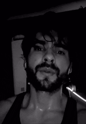 a man with a beard is sweating in a black tank top .