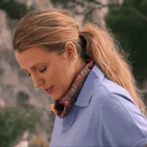 a woman wearing a blue shirt and a scarf around her neck looks down