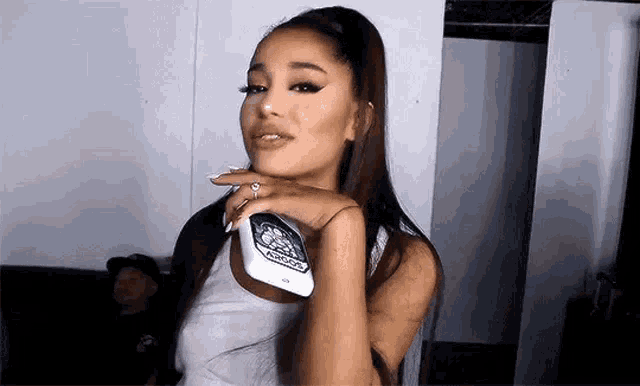 ariana grande is holding a cell phone in her hand and smiling .