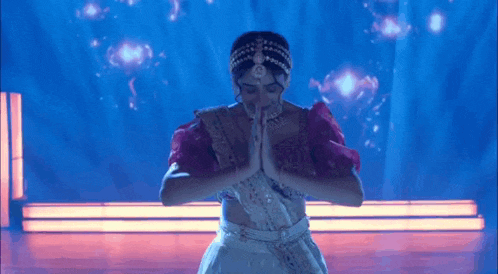 a woman is dancing on a stage with her hands folded in front of her face .