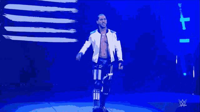 a man in a white jacket is walking on a stage in front of a wwe logo