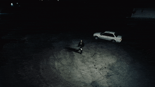 a man standing next to a white car in a dark parking lot