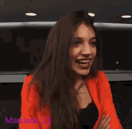 a woman wearing an orange jacket is laughing with the name murciano 21 written on the bottom