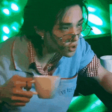 a man wearing glasses is holding a cup of coffee and making a funny face .
