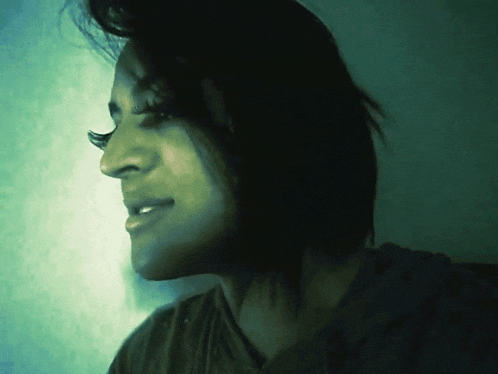 a close up of a woman 's face in a dark room with a green background