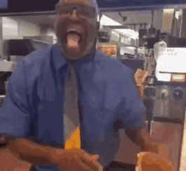 a man in a blue shirt and tie is standing in a kitchen with his tongue hanging out .