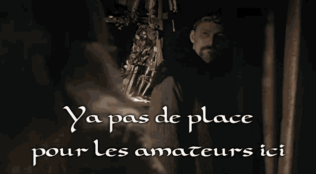 a man with a beard stands in a dark room with the words ya pas de place pour les amateurs ici written below him