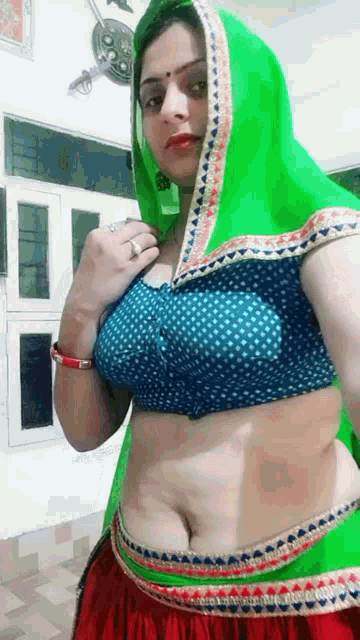 a woman wearing a green saree and a blue polka dot blouse is posing for a picture .