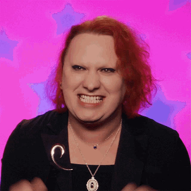 a woman with red hair is smiling and wearing a necklace with the letter g on it