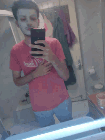 a man wearing a pink shirt that says coca cola takes a picture of himself in a mirror