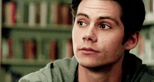 a close up of a young man 's face with a bookshelf in the background .