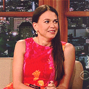 a woman in a red dress is smiling while sitting on a couch