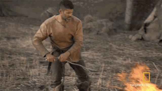 a man is standing in front of a fire with a national geographic logo in the corner