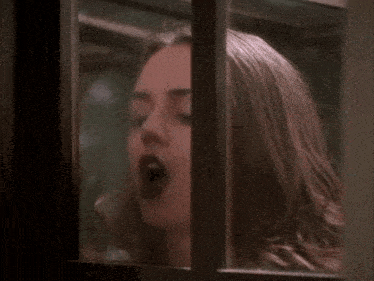 a woman looking out of a window with her hand on her nose