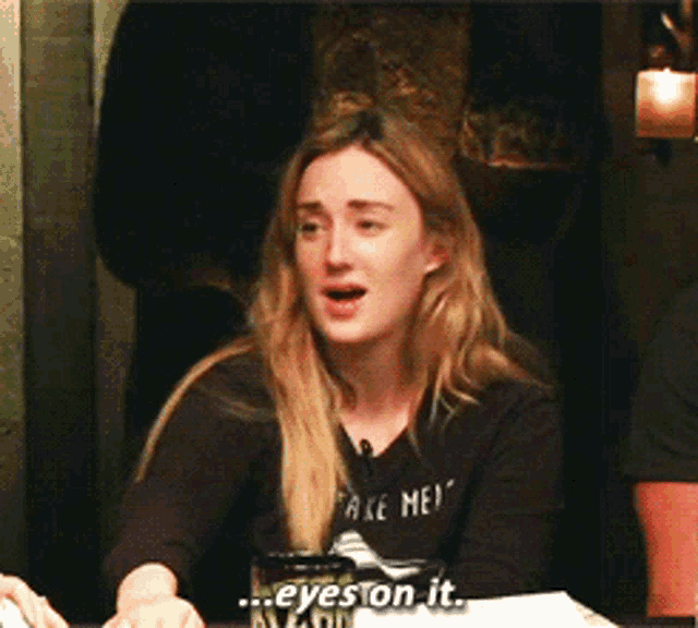a woman wearing a black shirt that says " take me " is sitting at a table