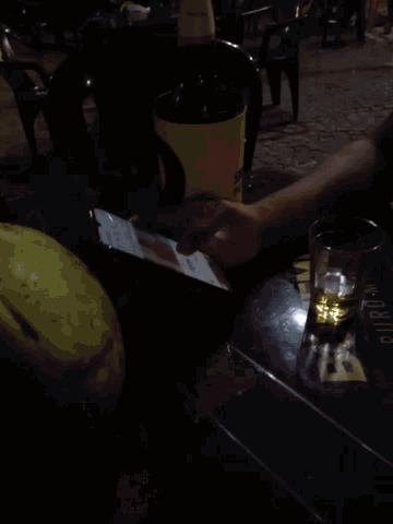 a person sitting at a table with a phone and a glass of beer on it
