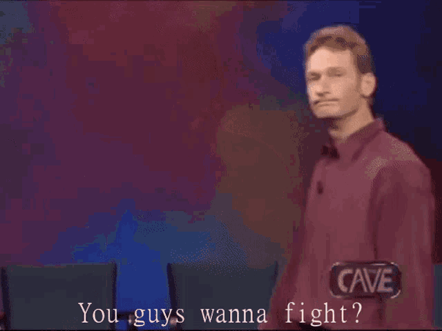 a man in a red shirt stands in front of a sign that says " you guys wanna fight "