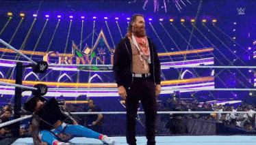 a man with a beard is standing in a wrestling ring with a fireworks display in the background