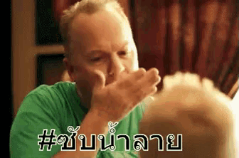 a man in a green shirt is covering his mouth with his hands while looking in a mirror .