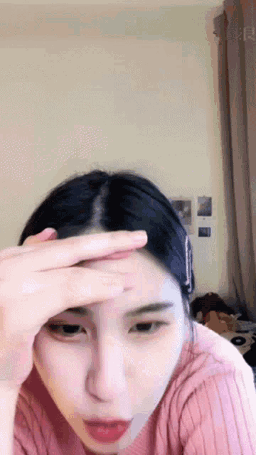 a woman in a pink sweater is holding her hand to her forehead