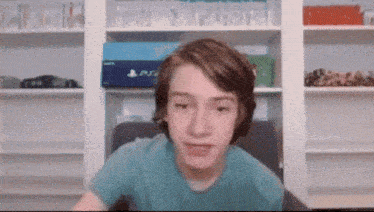 a boy in a blue shirt is looking at the camera in front of a playstation box