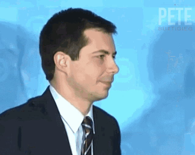 a man in a suit and tie stands in front of a blue background with the word pete on it