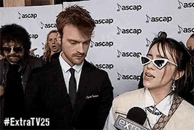 a man in a suit and tie is standing next to a woman wearing sunglasses .