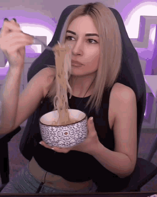 a woman in a black tank top is eating noodles from a bowl