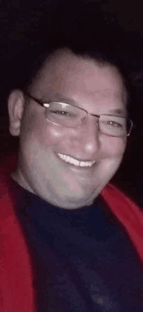 a man wearing glasses and a red sweater is smiling for the camera .