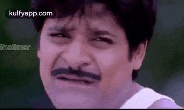 a man with a mustache is making a funny face and looking at the camera .