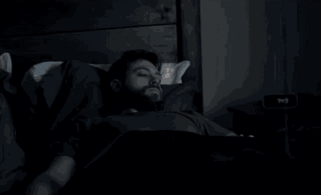 a person laying in bed looking out a window with blinds