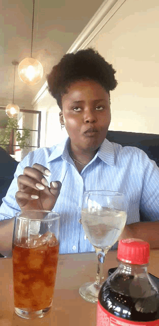 a woman sits at a table with a bottle of coke and a glass of water