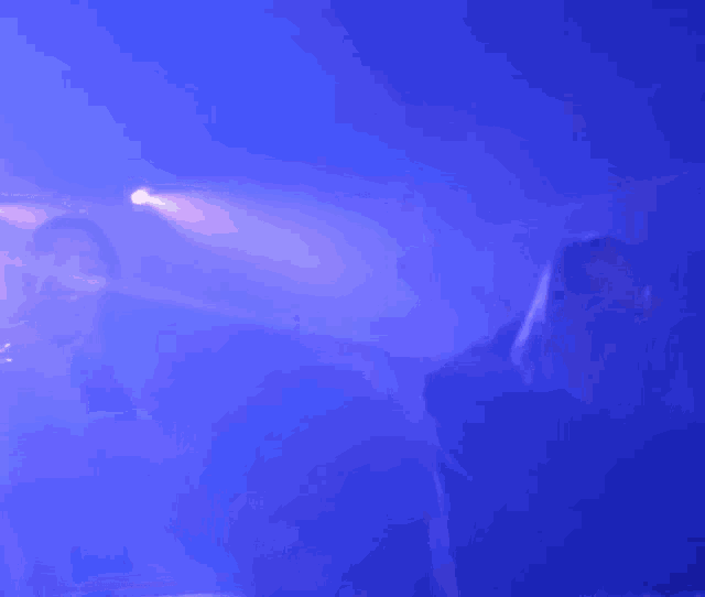 a man singing into a microphone in a dark room with blue lights behind him