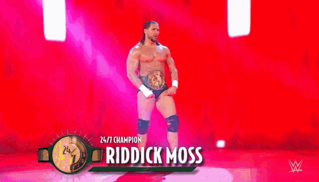 a wrestler is standing on a stage wearing a belt and knee pads .