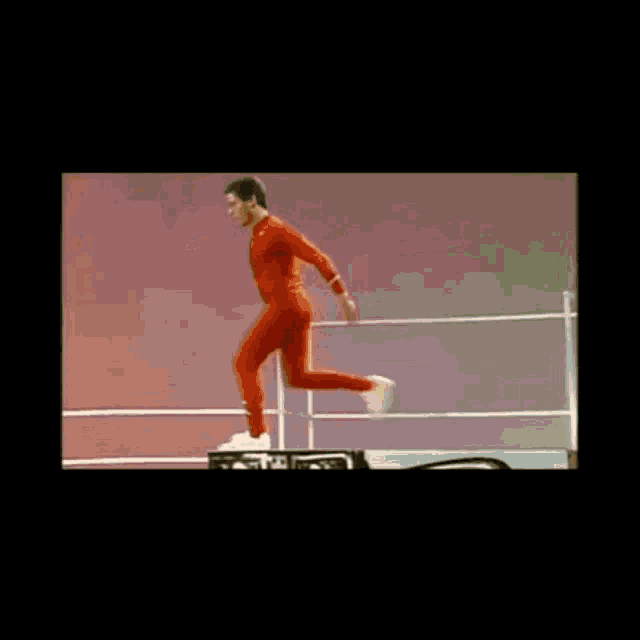 a man in a red jumpsuit is jumping in a boxing ring .