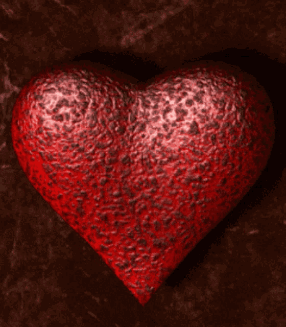 a red heart is sitting on a brown surface with a dark background