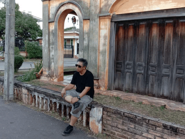 a man sits on a brick wall in front of a wooden garage door