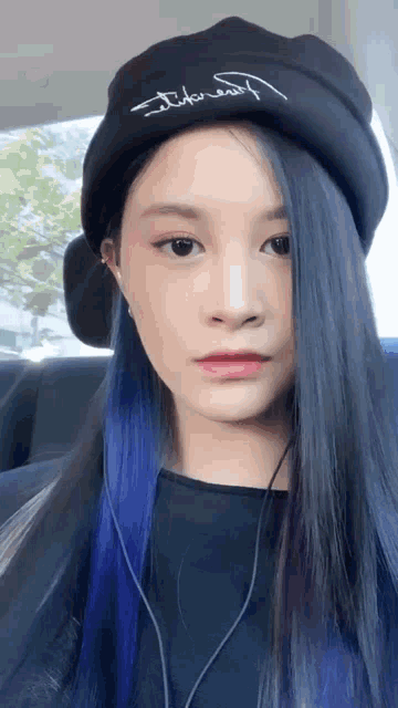 a woman with blue hair wearing a black beanie that says ' i like myself ' on it