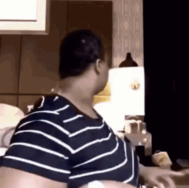 a woman in a striped shirt is standing in a bedroom .