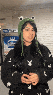 a woman wearing a green frog hat and a black playboy hoodie