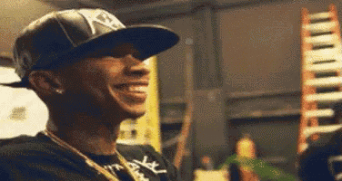 a man wearing a hat and a black shirt is smiling in a room .