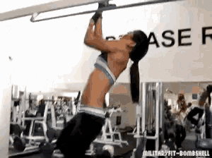 a woman is doing pull ups in a gym with a sign that says ase on it