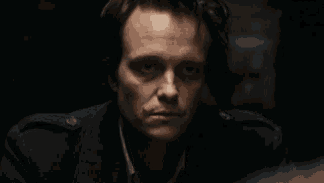 a close up of a man 's face in a dark room looking at the camera