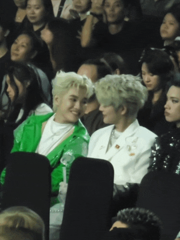 a man in a green jacket sits next to a man in a white suit