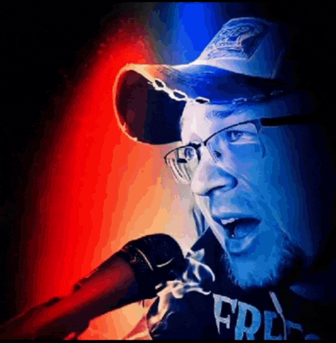 a man wearing a hat and glasses singing into a microphone with the word free on his shirt