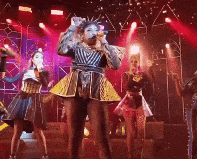 a woman singing into a microphone on a stage with other people