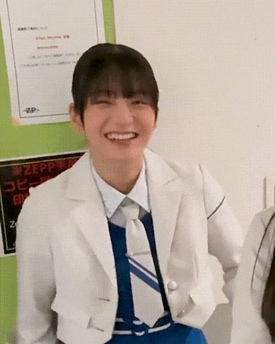 a woman in a white jacket and tie is smiling in front of a sign that says zepp