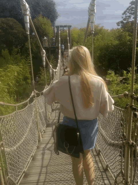 a woman in a pink sweater is walking across a hanging bridge