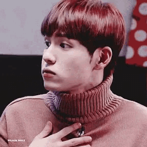a young man with red hair is wearing a pink turtleneck