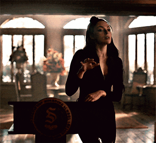 a woman in a black dress stands in front of a podium that has a circle with the letter s on it